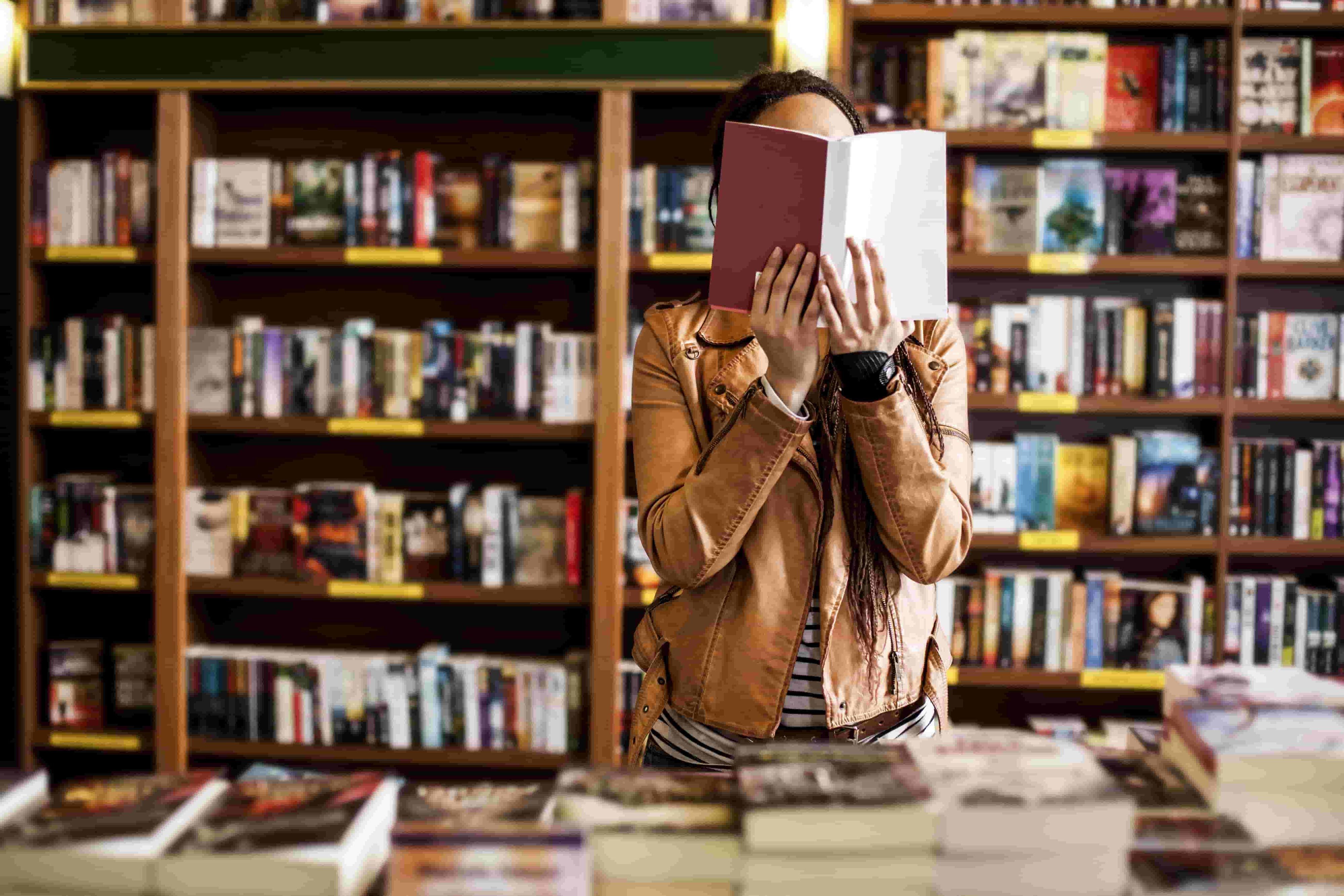 Woman holding open book in front of her face at book store